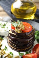Tasty grilled eggplant slices with tomatoes, pesto and yoghurt on table, closeup