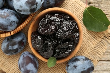 Dried prunes and fresh plums on wooden table, flat lay