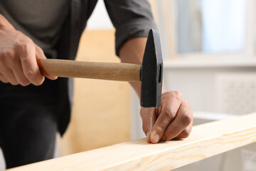 Man hammering nail into wooden plank indoors, closeup