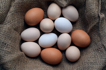 Top down view of assorted chicken eggs of various sizes and colors arranged on a rustic burlap fabric. Natural farm fresh food and organic protein concept