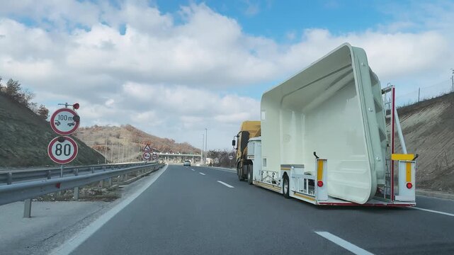 Long haul truck carrying large fiberglass swimming pool on flatbed trailer along a clear highway under a blue sky with scattered clouds