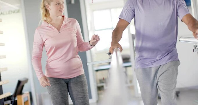Therapist checking tracker, guiding patient walking on bars with floating graphics tracking rehab