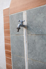 A closed outdoor tap with a hosepipe attachment. Garden tap outside on a tiled garden wall.