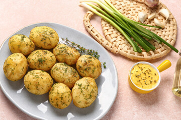 Plate of boiled baby potatoes with dill and green onion on pink background