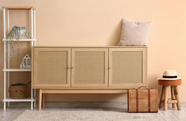 Interior of cozy living room with wooden chest of drawers and shelving unit near beige wall