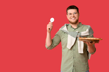 Young man with tasty pepperoni pizza and cutter on red background