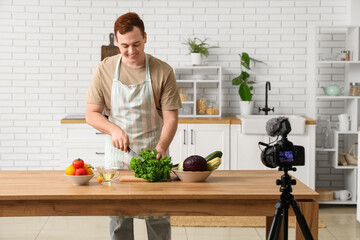 Young man with fresh vegetables recording cooking video in kitchen