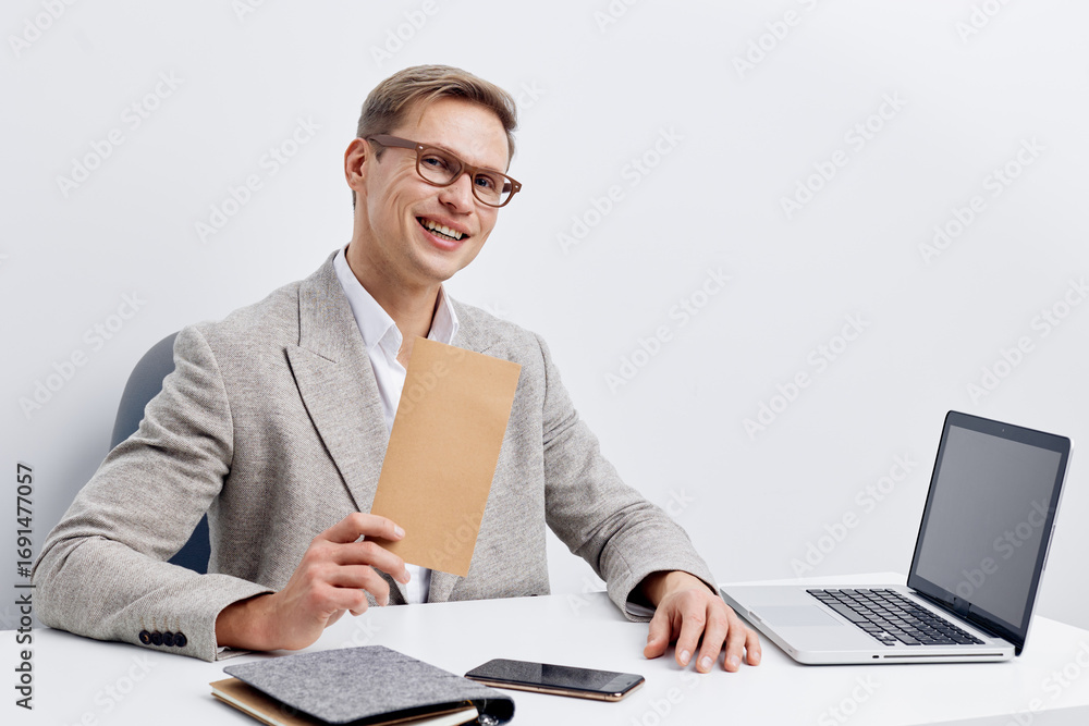 Poster smiling professional man in smart casual attire holding a notebook while sitting at a desk with a la