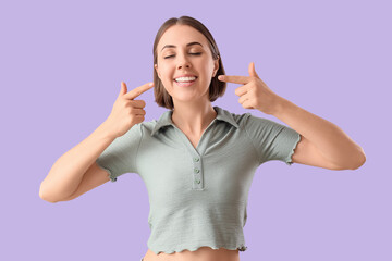 Young woman pointing at her teeth with occlusal splint on lilac background