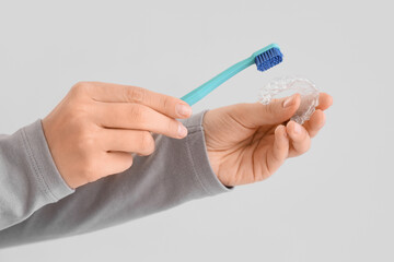 Female hands cleaning occlusal splint with toothbrush on light background