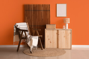 Chair, cabinet and folding screen near orange wall in interior of living room