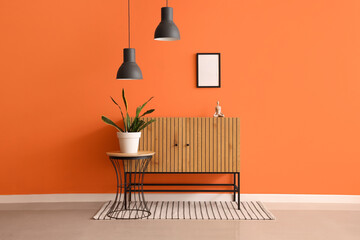 Wooden cabinet and houseplant on table near orange wall in interior of room
