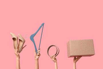 Female hands with wardrobe box, belt, hanger and high heels on pink background