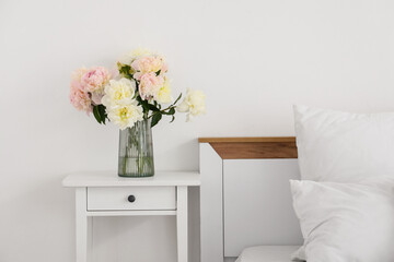 Interior of stylish bedroom with cozy bed and beautiful peonies on bedside table