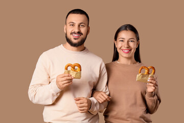 Fototapeta premium Happy couple holding pretzels in paper bags, smiling together on brown background, snack food and relationship