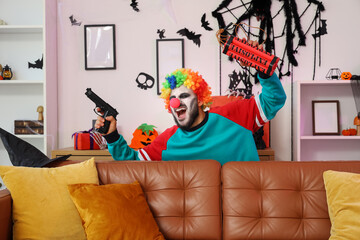 Young man dressed as crazy clown for Halloween with gun screaming while throwing dynamite in...