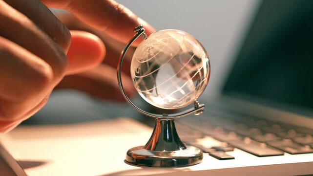 Spinning a globe while working on a laptop symbolizes global connectivity, digital exploration, remote collaboration, cross-border learning, and innovation in a tech-driven world.
