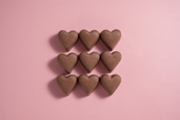 Heart-shaped chocolate pieces over pink background, abstract food love background
