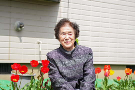A woman is sitting in a garden with red flowers. She is smiling and looking at the camera