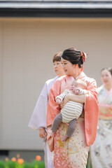 A woman in a pink kimono is holding a baby. The baby is sleeping and the woman is smiling. The scene is peaceful and heartwarming