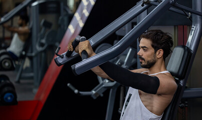 Caucasian man with strong and muscular body training on chest press machine in gym for muscle...