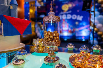 Elegant glass jar filled with golden candies on a decorated dessert table with sweets and chocolates in a festive event.