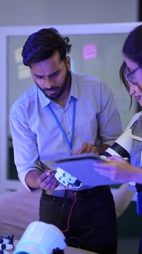  robotics engineers collaborate on a humanoid prototype, integrating sensors and actuators. They are programming the robot's AI and control logic using a tablet-based IDE