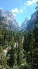 Fototapeta premium Stunning mountain landscape with verdant valley, river, and towering peaks under a bright, cloudy sky