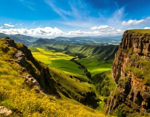 Obraz premium Dramatic cliff face overlooking a vibrant green valley and yellow fields