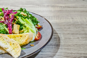 Close up view of chicken garlic salad on wooden table. Fresh vegetables in secret garlic sauce serve with chicken grill and garlic bread. Plate. Half. Copy space, empty, free, negative.