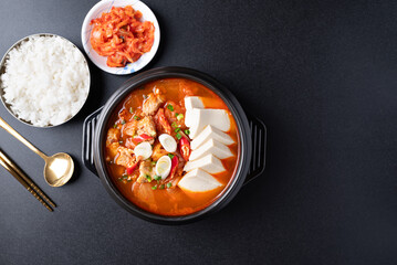 Korean food (Kimchi Jjigae), Kimchi soup with tofu and pork in Korean stone bowl eating with cooked rice and kimchi on black background