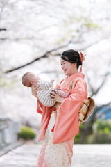 A woman in a kimono is holding a baby. The baby is smiling and the woman is smiling back. The scene...