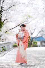A woman in a kimono is holding a baby. The baby is smiling and the woman is smiling back. The scene...