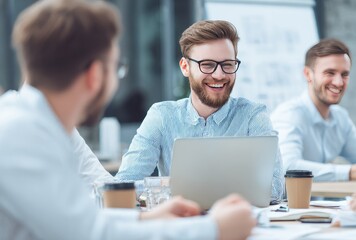 Obraz premium A group of young professionals around a table, one with glasses and a light blue shirt laughing, laptop and disposable cups, looking engaged and happy