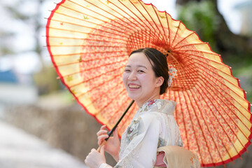 A woman is smiling under a large red and yellow umbrella. The umbrella is open and the woman is...