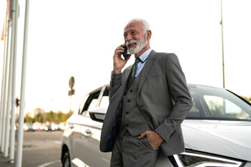 Senior businessman talking on phone near car in city