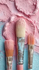Close-up of three paintbrushes resting on swirls of textured pink and blue paint, creating an artistic and tactile composition