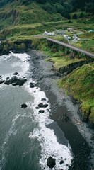 Coastal vista with a bridge spanning a rocky beach and lush, green cliffsides, meeting a distant tree-covered hill under an overcast sky