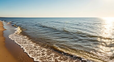 Gentle ocean waves kiss a sandy shore under a clear sky, reflecting sunlight's golden shimmer.