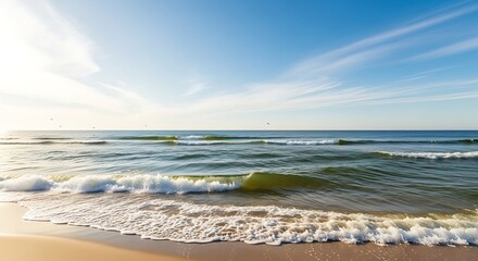 Gentle ocean waves roll onto a serene sandy beach under a clear blue sky with wispy clouds