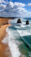 Cliffside vista over a sandy beach meeting turbulent turquoise ocean waves under a blue sky speckled with cumulus clouds