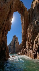 A sunlit arch of eroded rock formations over a body of water, showcasing textures of stone and rippling water, under a clear blue sky