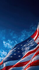 A vibrant American flag waves against a deep blue sky dotted with wispy white clouds, creating a patriotic and uplifting image