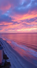 Coastal sunrise captures pink and orange clouds reflecting on the ocean's surface, meeting the sandy beach with gentle waves