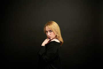 Fototapeta premium In the studio, against a dark background, a blonde-haired woman dressed in a black dress poses for a photographer for an advertisement.