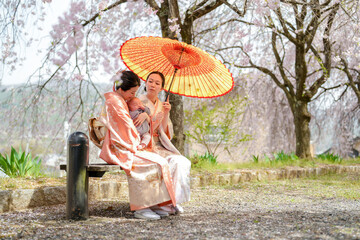 A woman sits on a bench with a baby in her arms and an umbrella over them. The scene is peaceful and serene, with the woman and baby enjoying the outdoors
