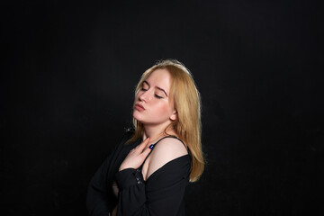 Fototapeta premium The woman is wearing a black dress with a black bra underneath. She stands against a dark background.