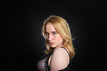 Naklejka premium The woman is wearing a black dress with a black bra underneath. She stands against a dark background.
