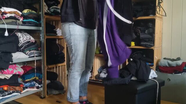 A woman in jeans folds used clothes, trying to bring order to her untidy, chaotic open wardrobe at home in Bern, Switzerland