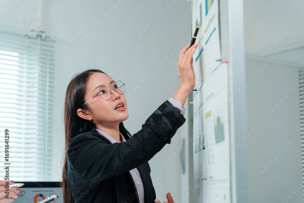 Poster businesswoman pointing at charts and graphs on a whiteboard during a dynamic presentation in the off